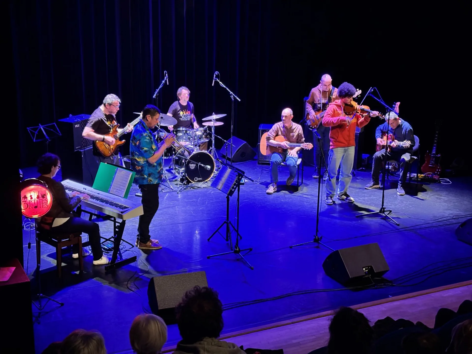 Groupe d’adultes jouant sur scène avec guitares, basse, batterie, clavier et violon
